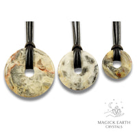 Natural cream shade crazy agate donut pendants in three sizes hanging from black vegan cords arranged left to right from large to small