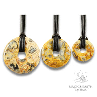 Natural yellow shade crazy agate donut pendants in three sizes hanging from black vegan cords arranged left to right from large to small