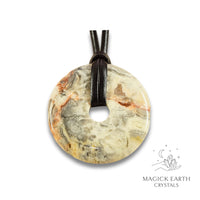 Natural 50mm cream shade crazy agate donut pendant hanging from a black vegan cord.