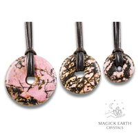 Natural rhodonite donut pendants in three sizes hanging from black vegan cords arranged left to right from large to small