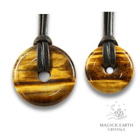 Natural tiger eye donut pendants in two sizes hanging from black vegan cords arranged left to right from large to small